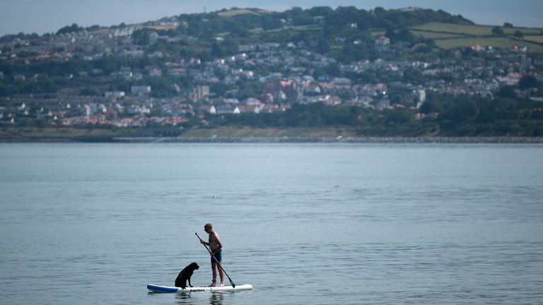A man stands on a paddleboard with his dog near the beach at Rhos-on-Sea, Wales. Pic: Reuters