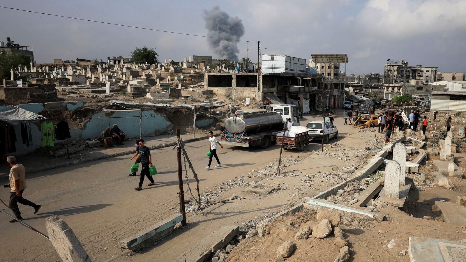 Palestinians walk past damaged graves as smoke rises following an Israeli strike in Gaza City. Pic: Reuters/Dawoud Abu Alkas