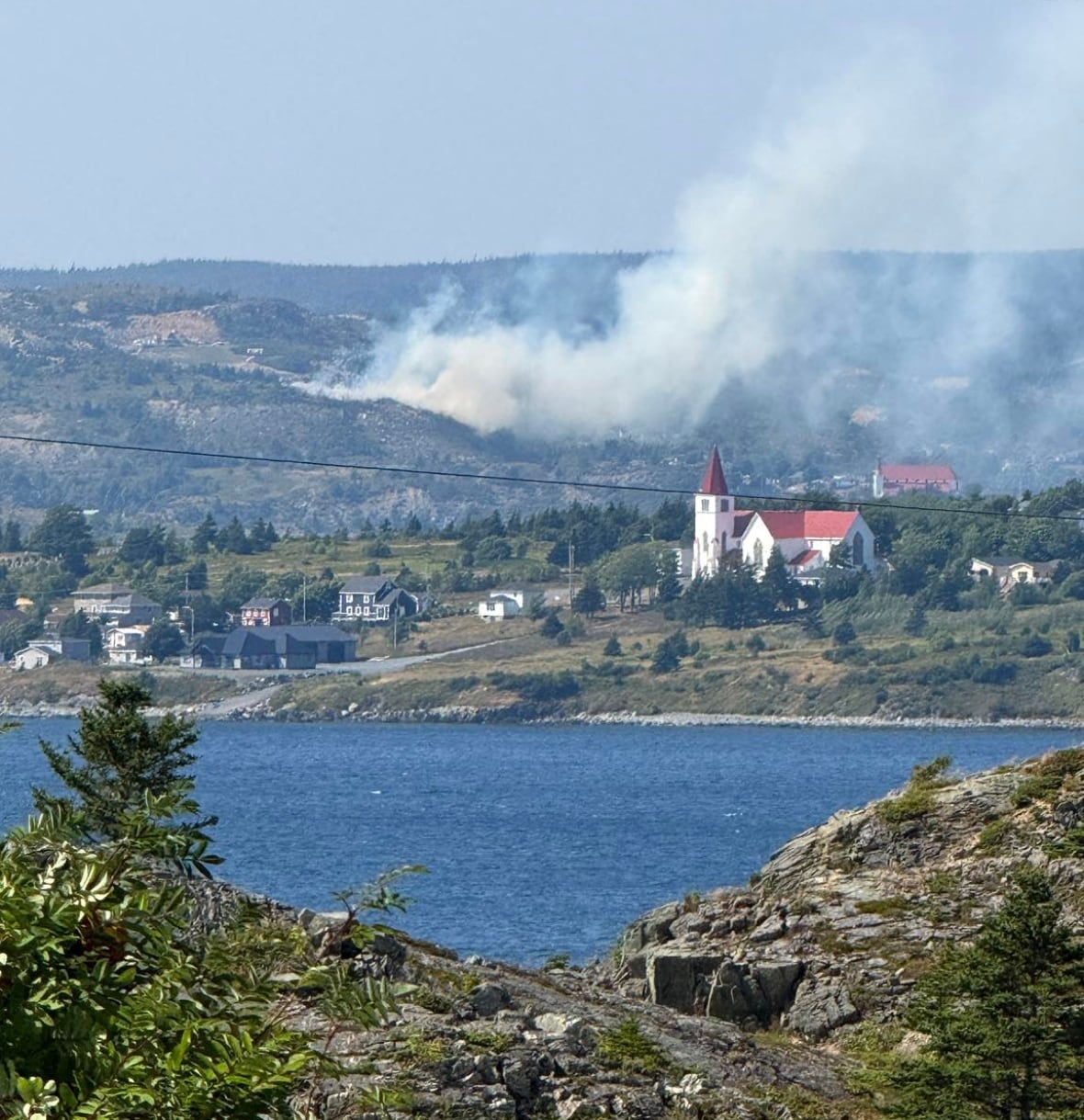 Smoke rising from a hill near water.