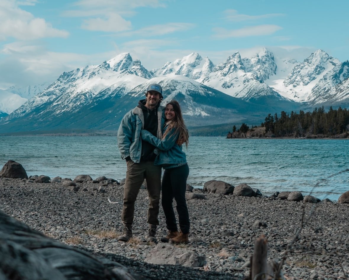 A couple poses next to picturesque mountains and a lake.