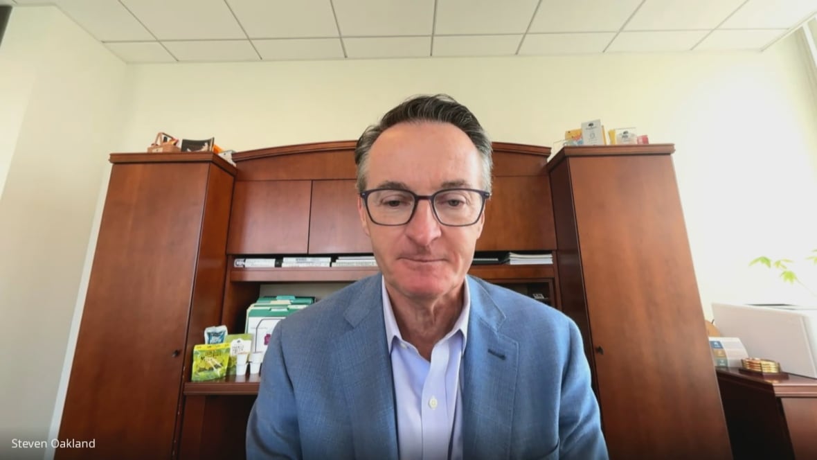 A man wearing glasses and a suit jacket sits in front of a desk.