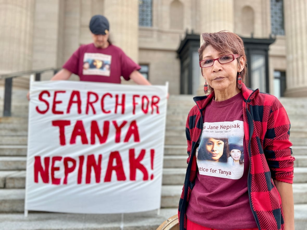 A woman stands at the bottom of large concrete steps and next to a person holding a sign that reads, 'Search for Tanya Nepinak.'