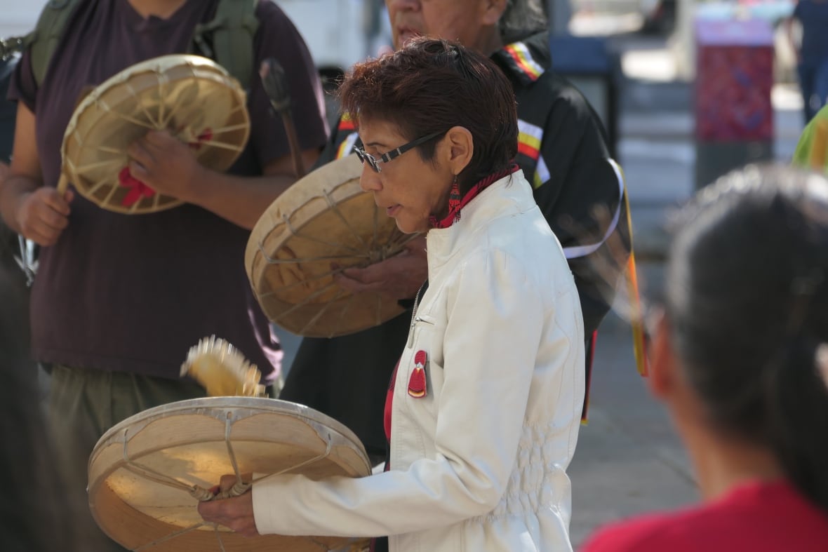 a woman wearing glasses drums on a traditional drum. 