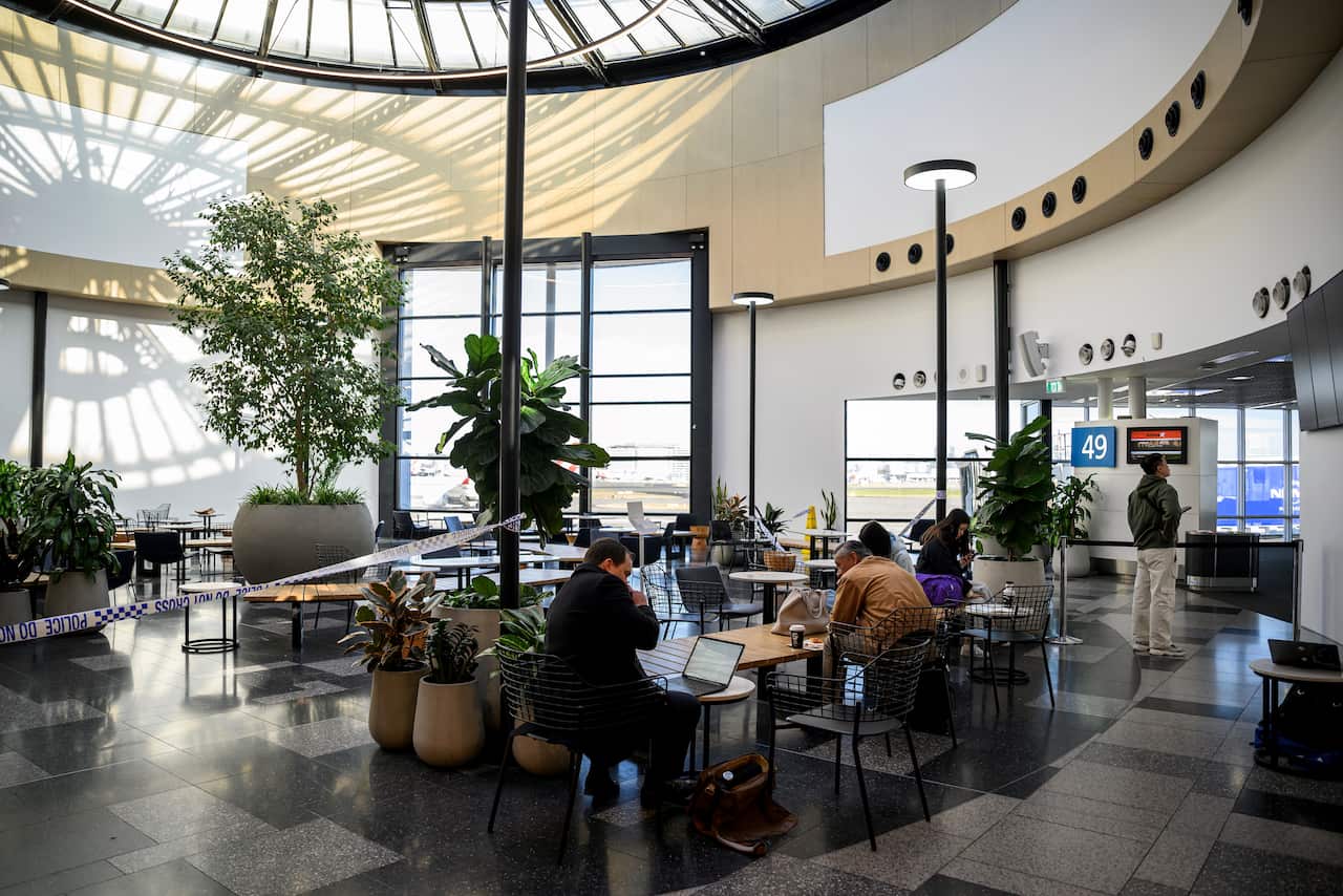 People sitting at tables in an airport terminal. There is police tape sectioning off a part.