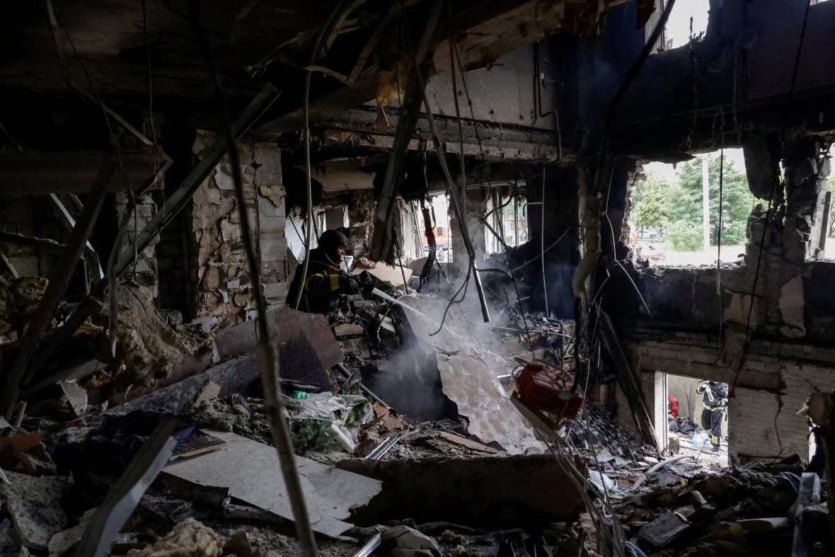 A firefighter is shown inside a heavily charred and destroyed room spraying water.