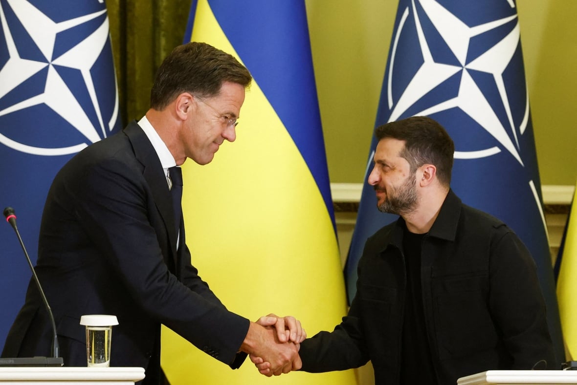Two men shake hands in front of a Ukrainian flag
