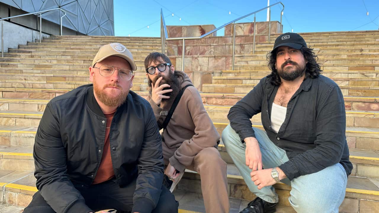 Three men with beards on a set of stairs in Federation Square in Melbourne.
