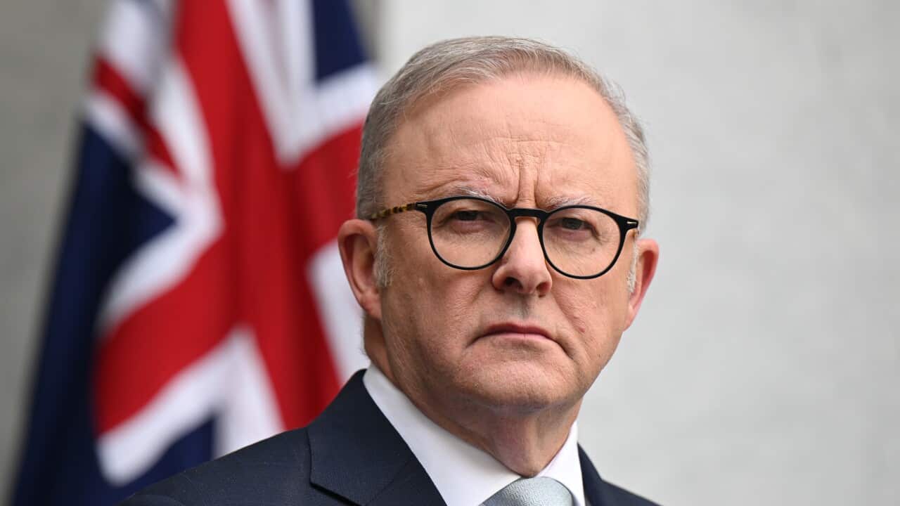 Anthony Albanese, in a suit, is standing in front of an Australian flag.