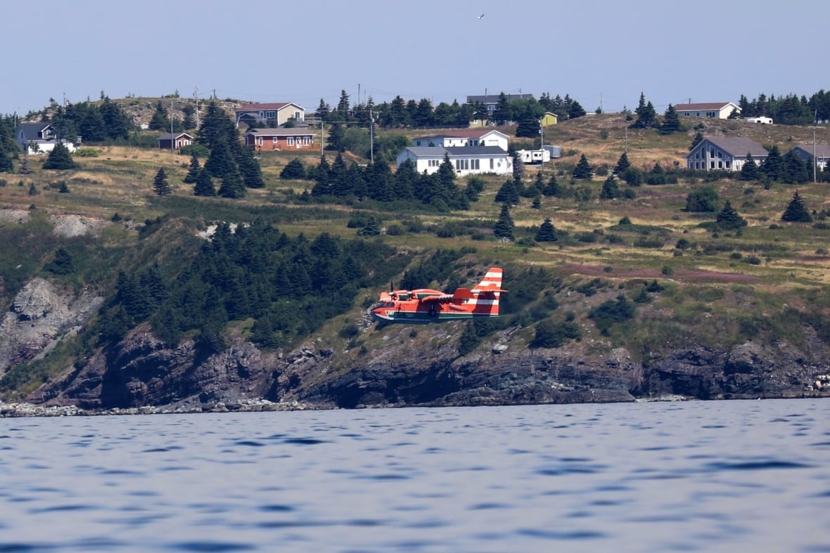 An orange plane flying over a body of water.