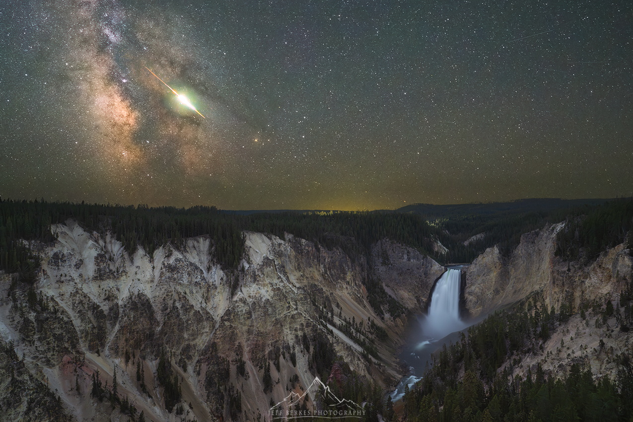 A bright meteor is pictured travelling across the glowing band of the Milky Way in a starry night sky above a waterfall at the head of a rocky canyon.