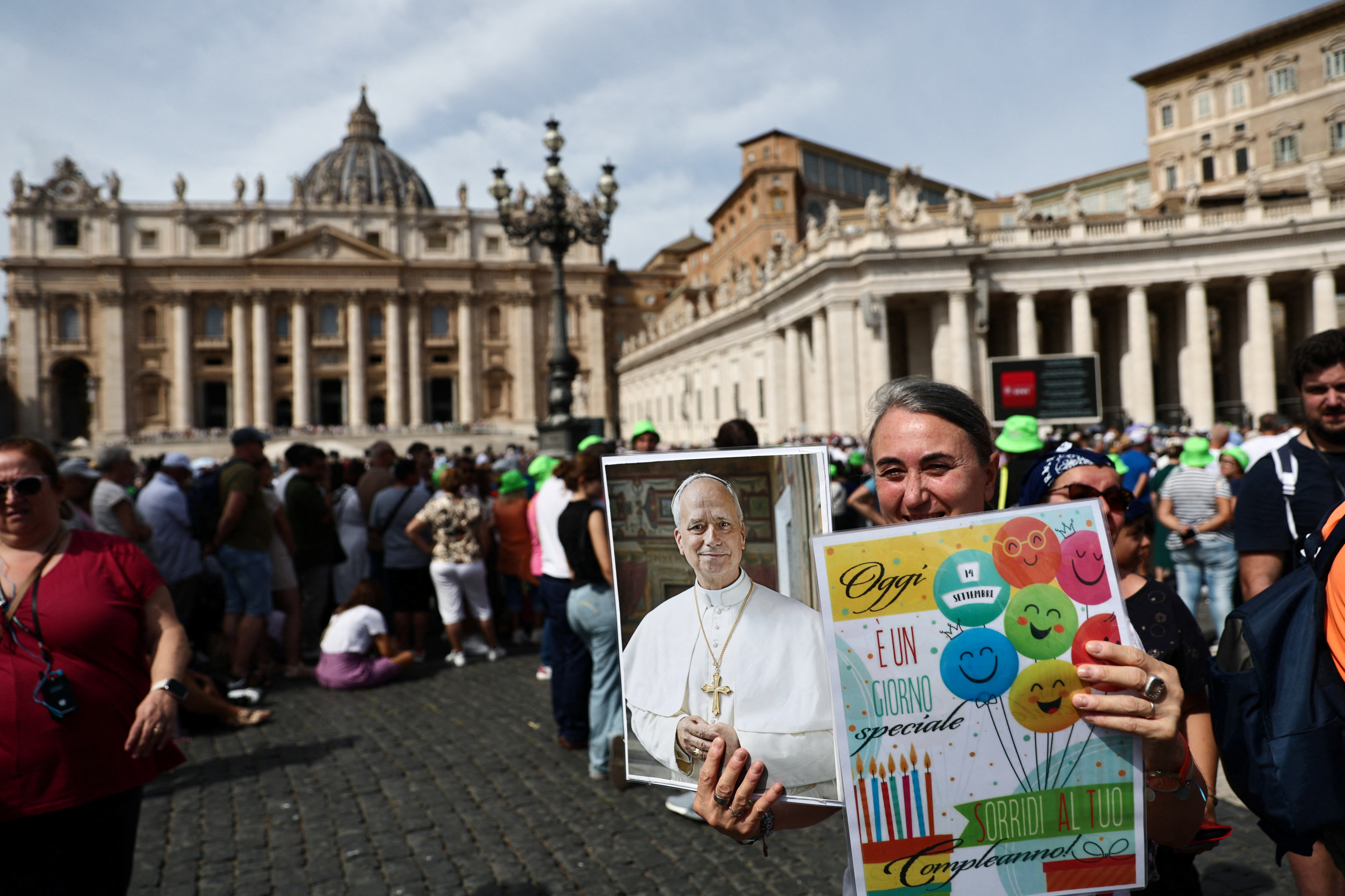 A person holds a portrait of Pope Leo XIV and a birthday card in St. Peter's Square.