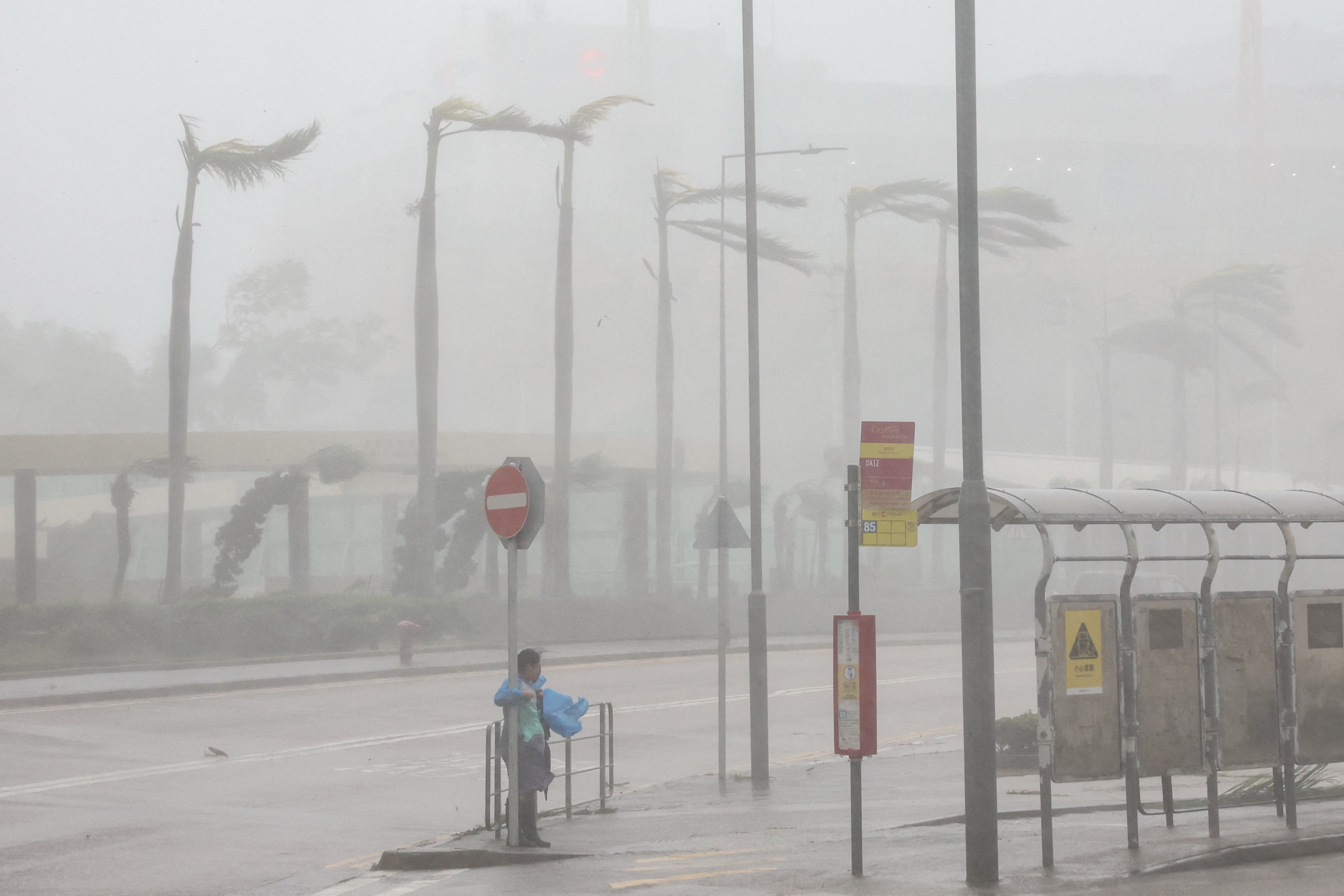 A woman in a blue rain jacket clings to a street sign post to maintain balance against strong winds from Super Typhoon Ragasa in Hong Kong.