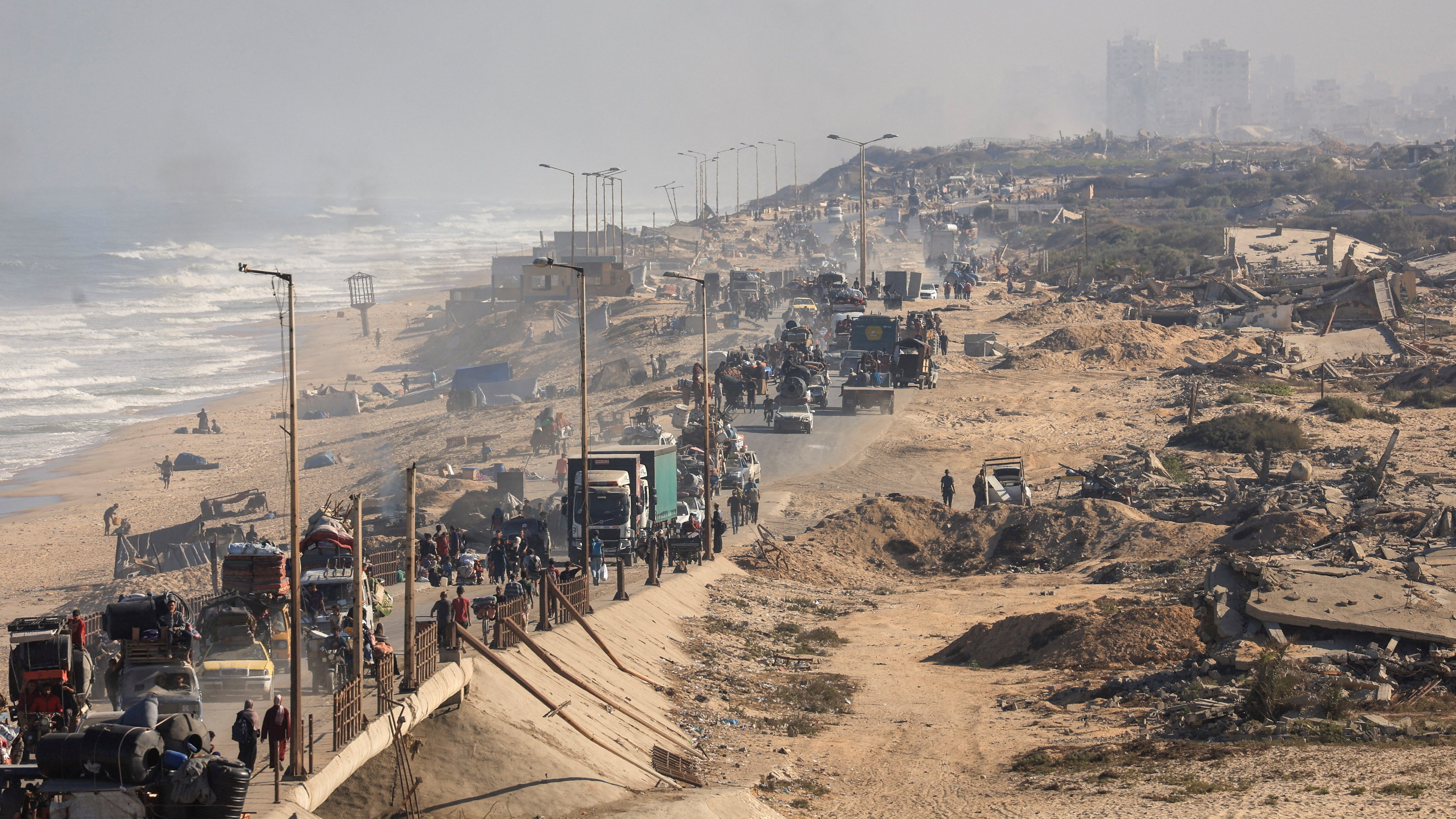Displaced Palestinians fleeing Gaza City, traveling south along a coastal road amidst destruction.