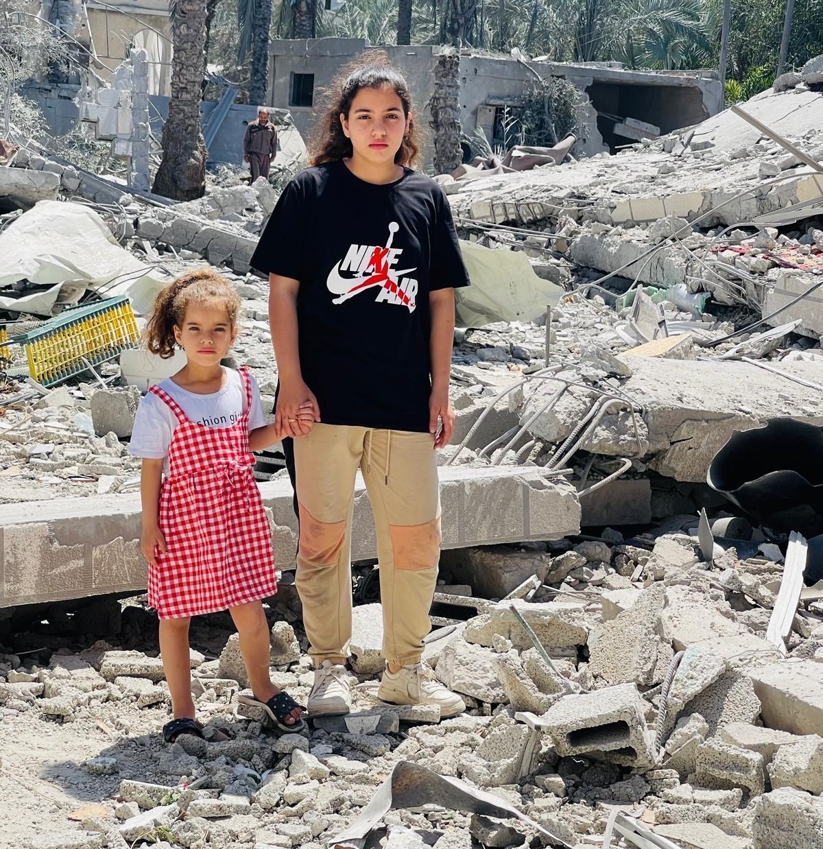 Two young girls stand amidst the rubble of a destroyed building in Gaza City.