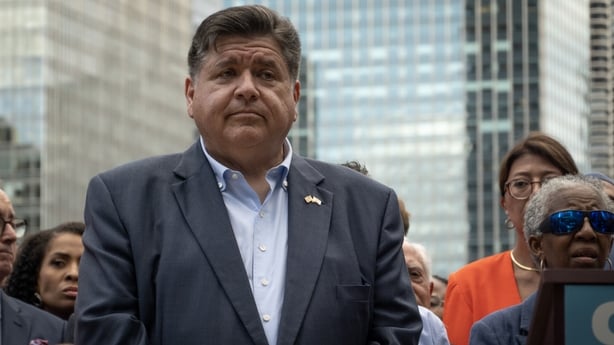 Illinois Governor JB Pritzker at a news conference surrounded by a crowd.