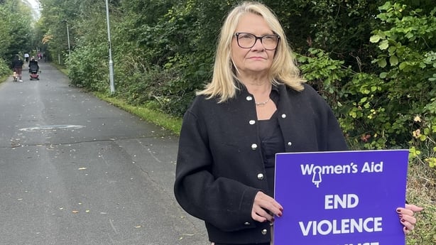 A woman stands in a road with a sign