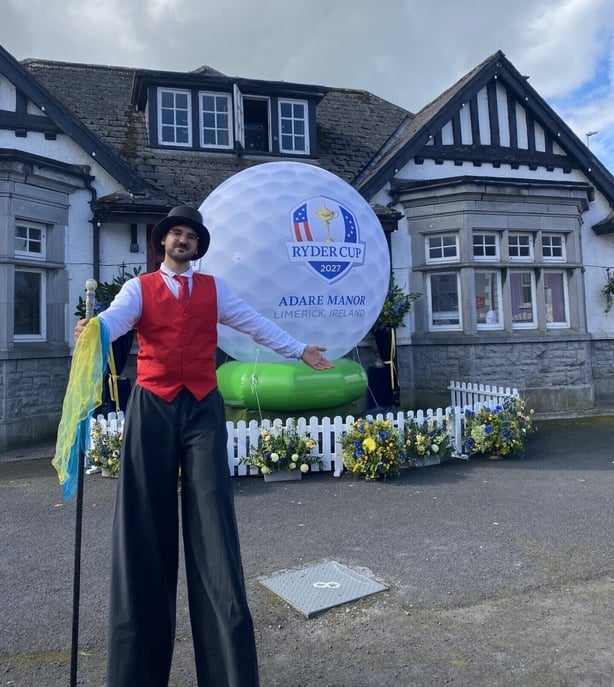 Man on stilts in front of a giant golf ball