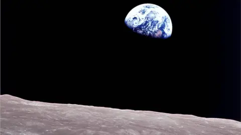 William Anders/Nasa A three quarters view of the Earth appearing as a blue marble with white swirls, rising above a lunar landscape