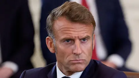 Getty Images A man with sideburns and a brooding but determined look, wearing a dark blue jacket and white shirt, looks into the distance