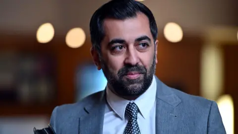 Getty Images Humza Yousaf has dark hair and a dark beard. He is wearing a light blue suit over a white shirt with a dark coloured tie.