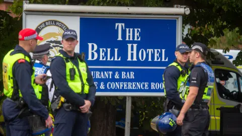 EPA/Shutterstock A blue sign with large white writing advertising a hotel is shown with five police officers standing in front of it and with police vans seen in the background.
