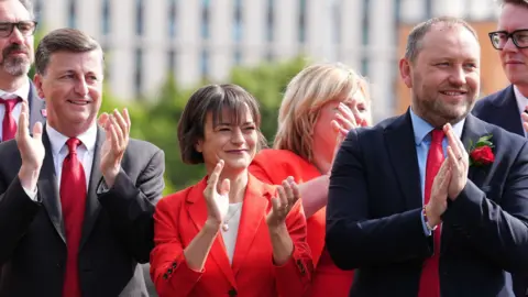 PA Media Alexander and murray in suits clap their hands with a woman in a red suit between them.