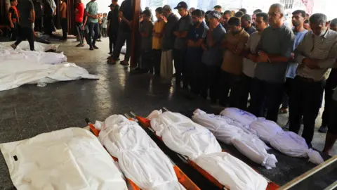 Reuters Mourners pray near the bodies of people reportedly killed in an Israeli air strike on a building where displaced families were sheltering, at al-Ahli hospital, Gaza City (24 September 2025)