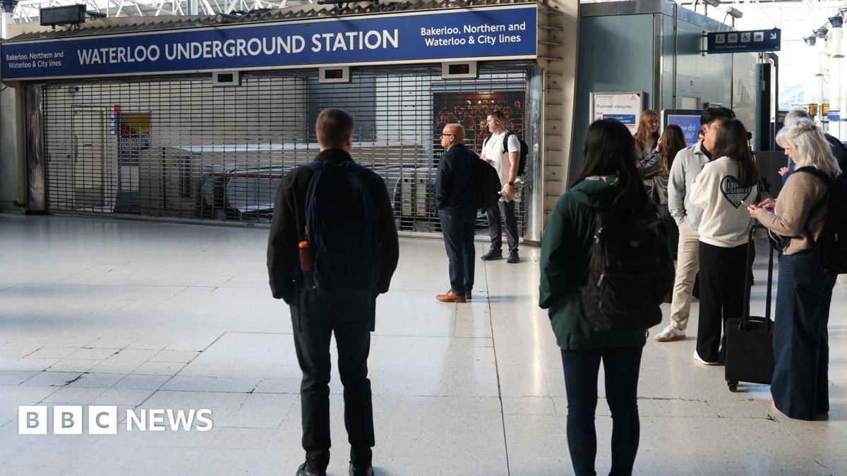 People standing in a train station concourse looking at a shuttered entrance to the Tube.