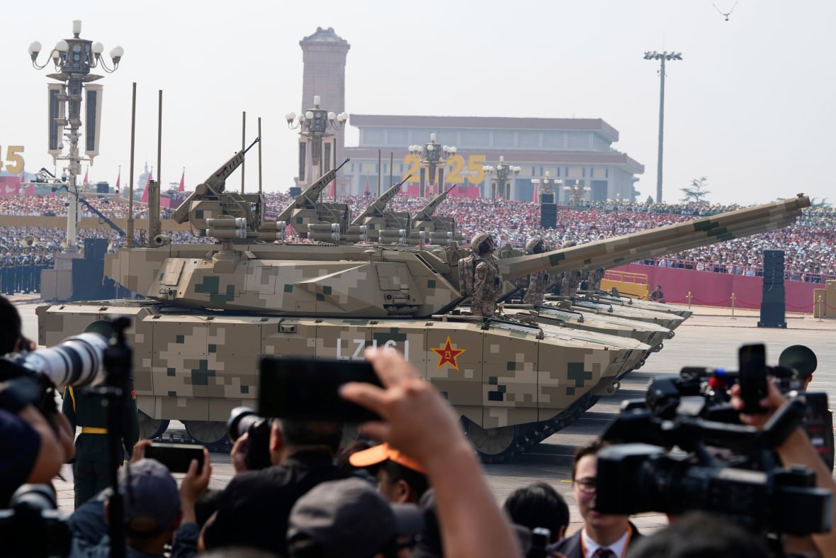 Tanks roll by as people in the crowd take photos.