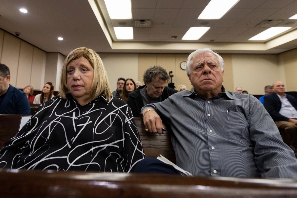An older man and woman are shown seated in what appears to be a courtroom.