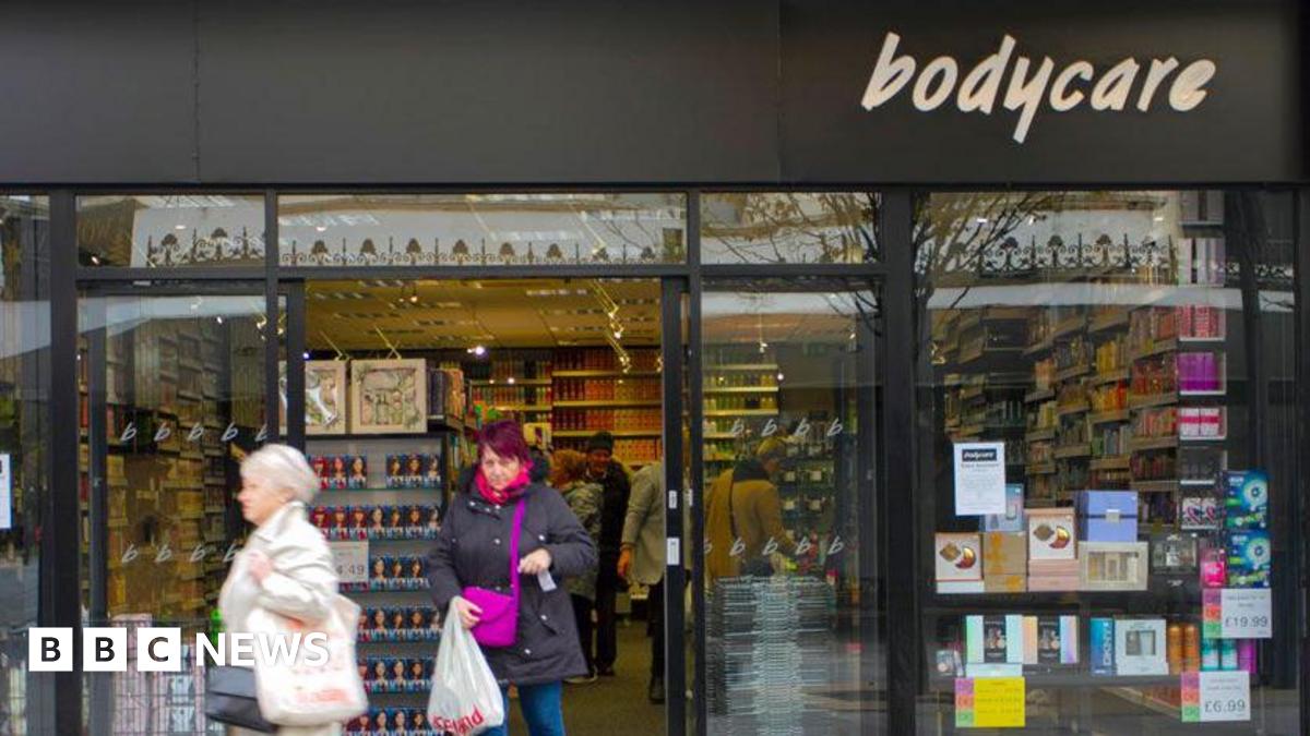 Two customers leave a Bodycare shop, where shelves and shelves of beauty and cosmetic products reach from the ceiling to the floor.