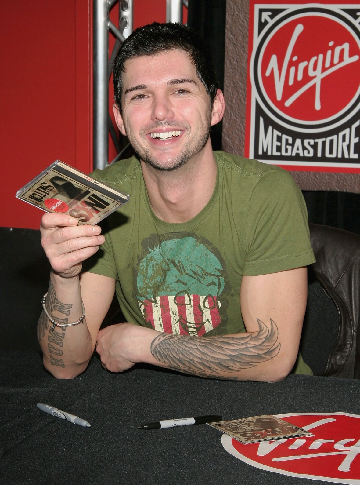A man with tattoos signs copies of a CD he sang on.