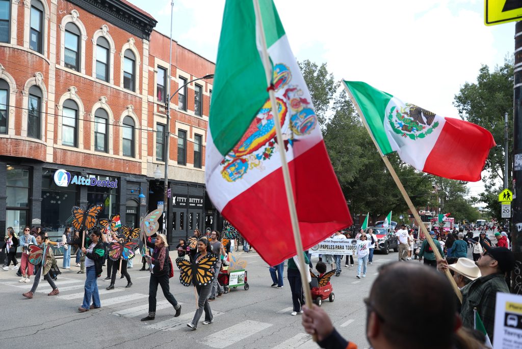 Marchers hold butterfly posters as they pass supporters waving Mexican flags during the Mexican Independence Day parade in Chicago’s Pilsen neighborhood on Saturday, Sept. 6, 2025.