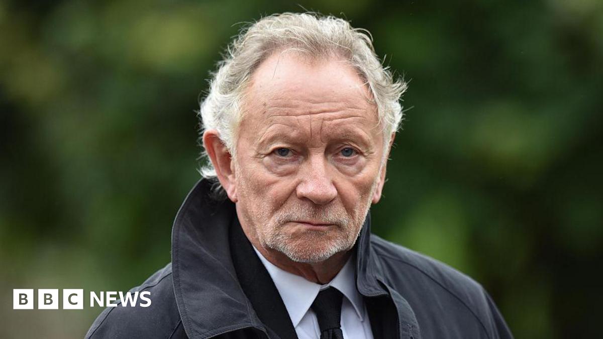 Phil Coulter. He has white wavy hair, wearing a black coat, white shirt and black tie.