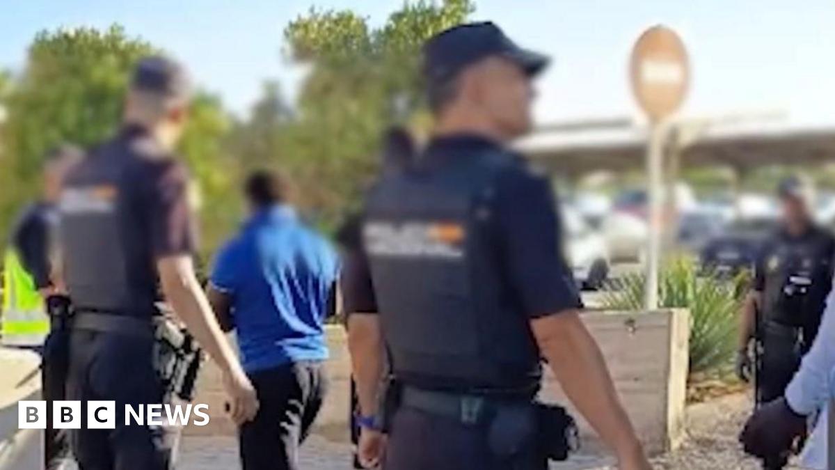 A police handout photo showing the backs of police with their faces blurred, standing next to a coach as people from the migrant boat exit it.