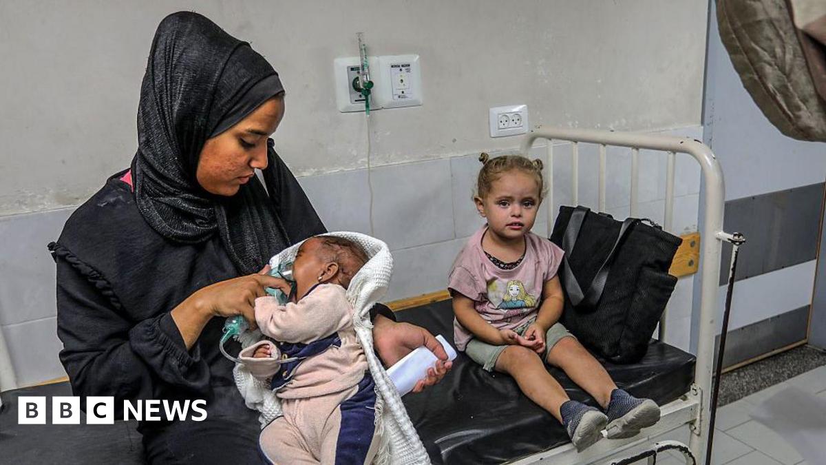 A Palestinian woman nurses a child in her lap on a hospital bed.