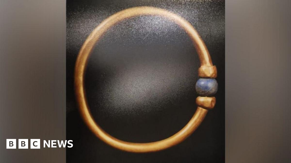 The bracelet is gold and adorned with a blue, round bead