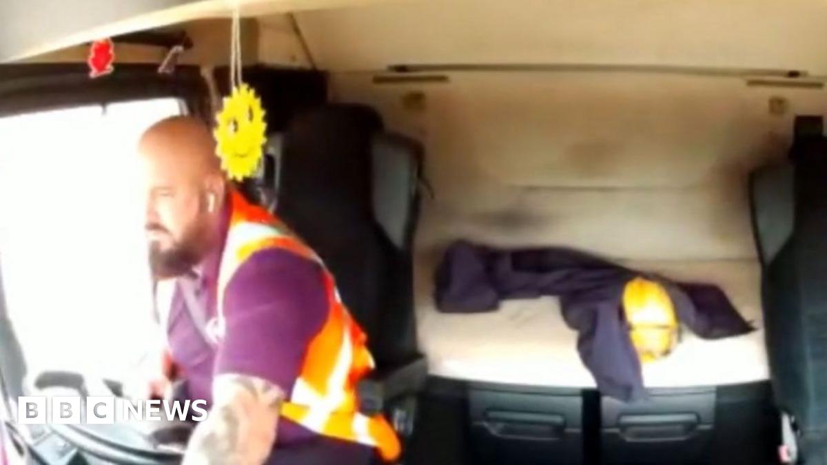 Neil Platt in the cab of his lorry with one hand on the wheel and one out of sight on his phone