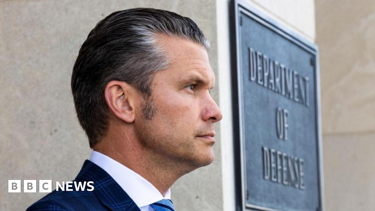 A file photo of Pete Hegseth standing in front of a sign which reads "Department of Defense"