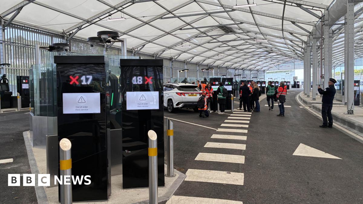 Two finger printing machines in the foreground of a hanger at Eurotunnel in Folkestone with cars and people in the background.