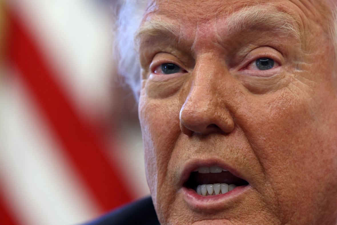 A close up of a man's face. An American flag can be seen in the background.