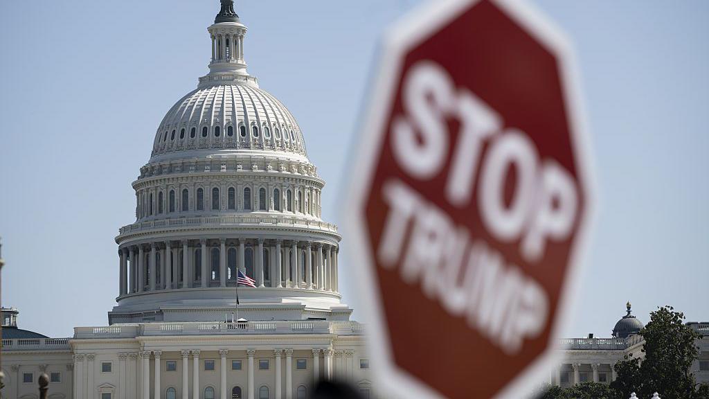 File image of the US Capitol building with a blurry sign in the foreground that reads "stop Trump"