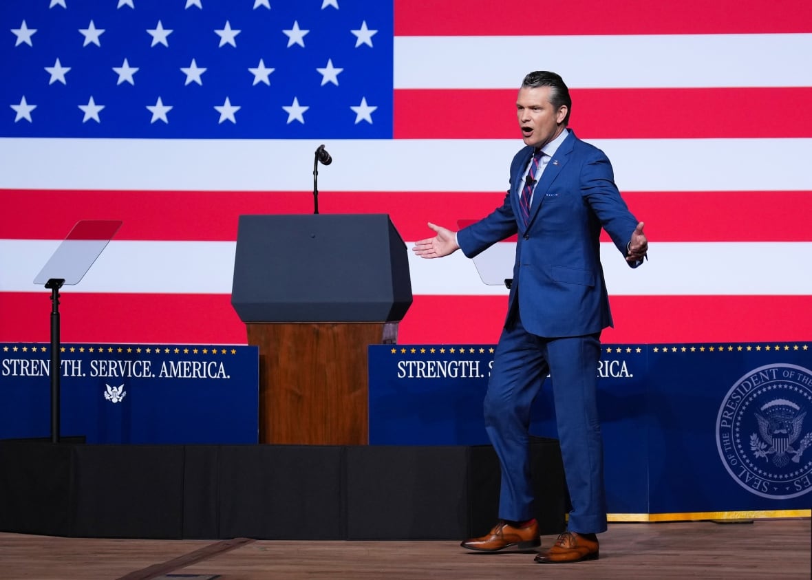 A man in a suit talks in front of a giant U.S. flag