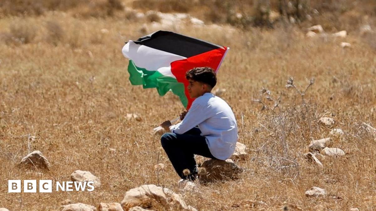 Close-up of a bearded man in black T-shirt standing next to a tree.