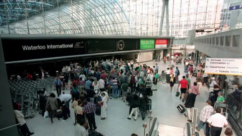 PA Media Waterloo International is full of people queuing and walking about. There are signs showing arrivals, departures and ticket desks. There is a clock showing 09.30 BST. The roof of the high building is made from glass.