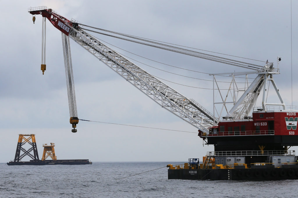 Construction crane floats next to a barge carrying jacket support structures and a platform for a turbine for a wind farm ...
