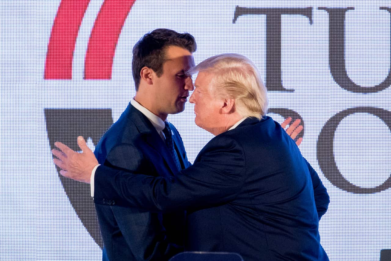 Donald Trump is embracing a man in a suit on a stage.