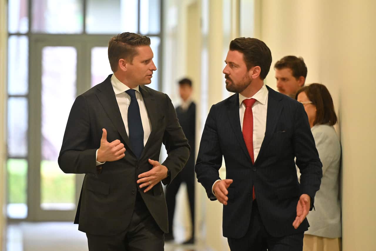 Two men in dark suits and ties walking through a hall, talking to each other