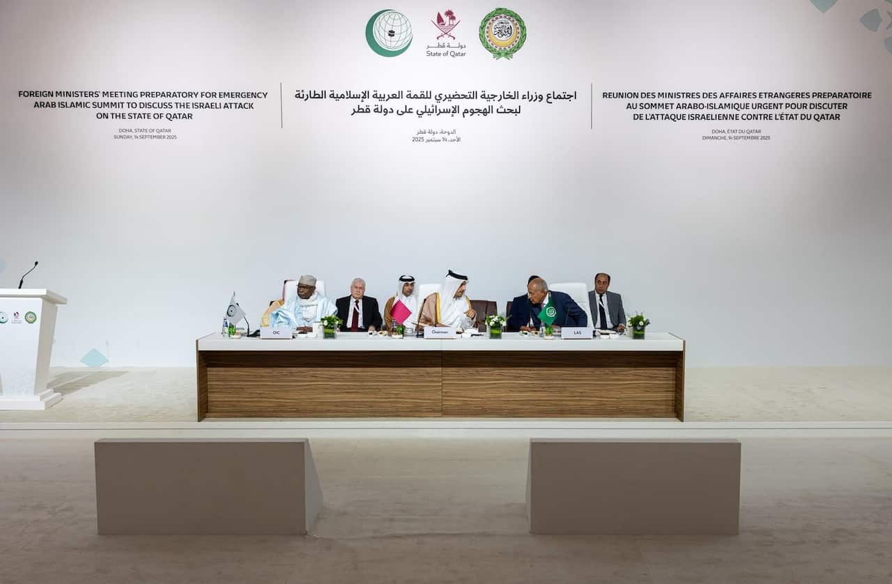 A group of men seated at a table. There is a podium next to them with a microphone.