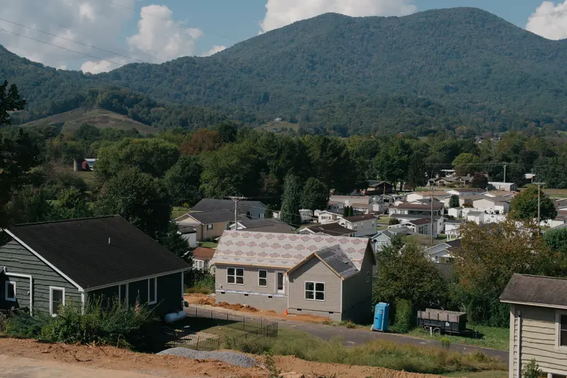 Homes sit at the base of looming mountains covered in trees.